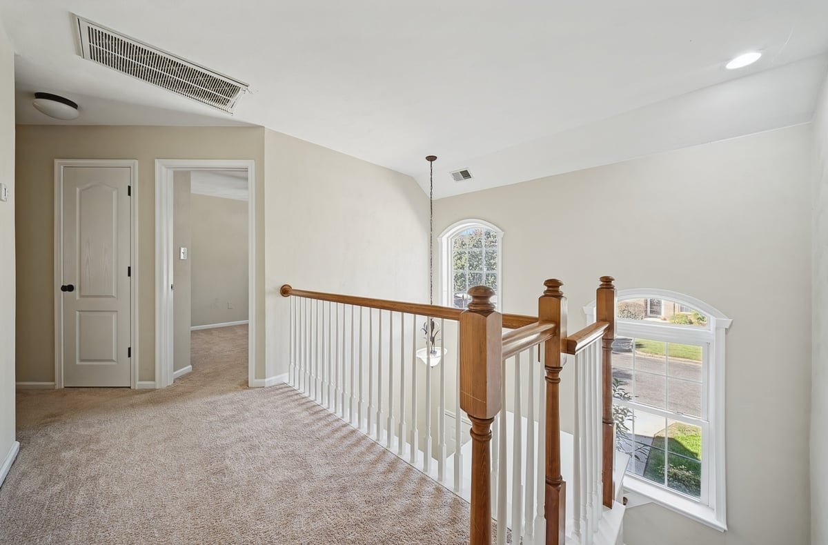 Bright upstairs hallway with white railings, wooden stair posts, beige carpet, and white doors leading to various rooms