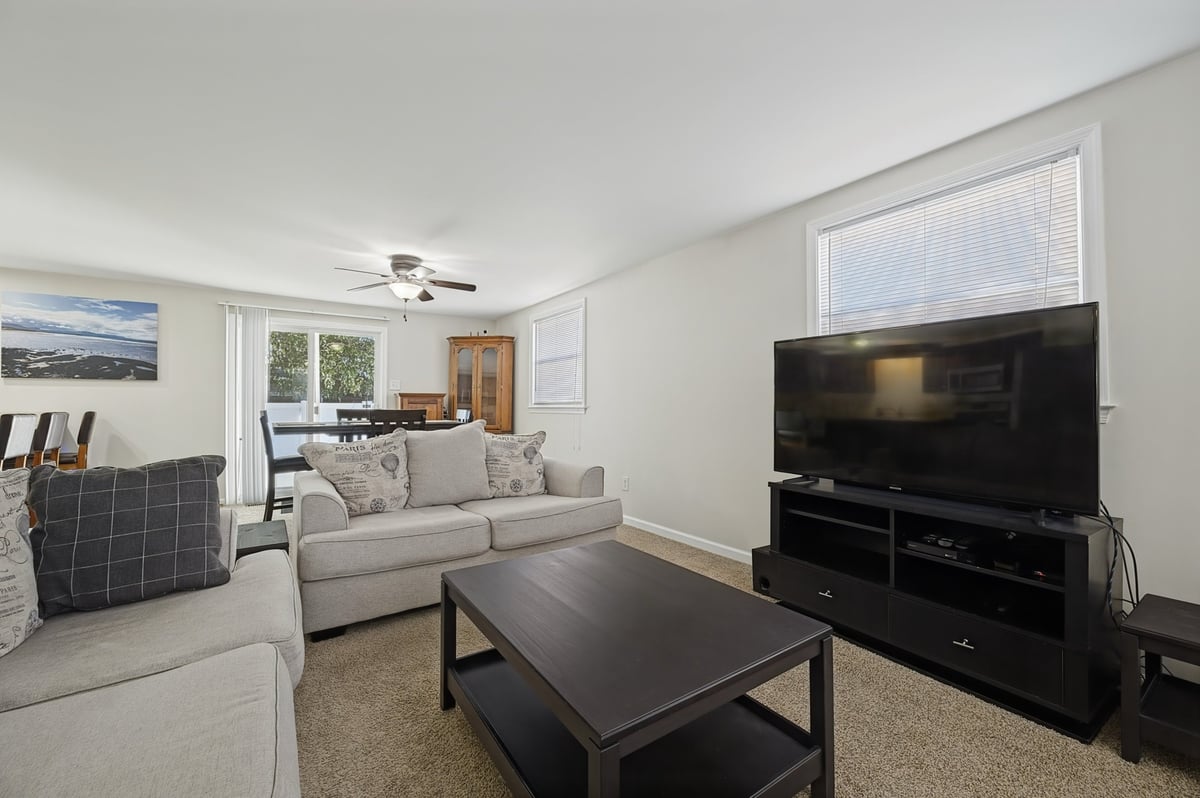 Modern living room with gray sofa, black TV stand, dark coffee table, and open floor plan connecting to kitchen and dining area
