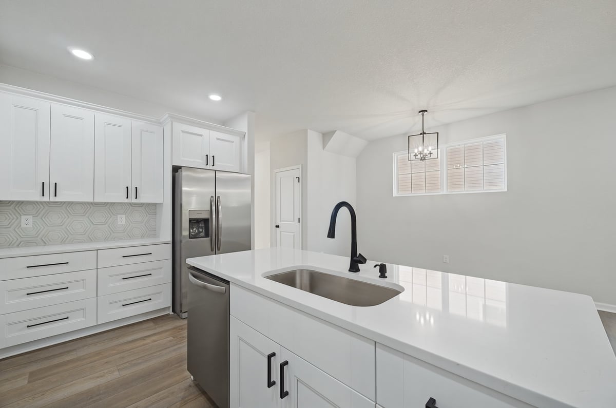 Modern white kitchen with island sink, stainless steel refrigerator, and recessed lighting