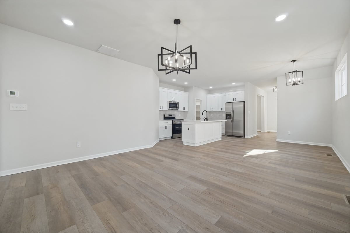 Bright modern open-concept home interior with wood flooring, white walls, kitchen with stainless steel appliances, and contemporary light fixtures.