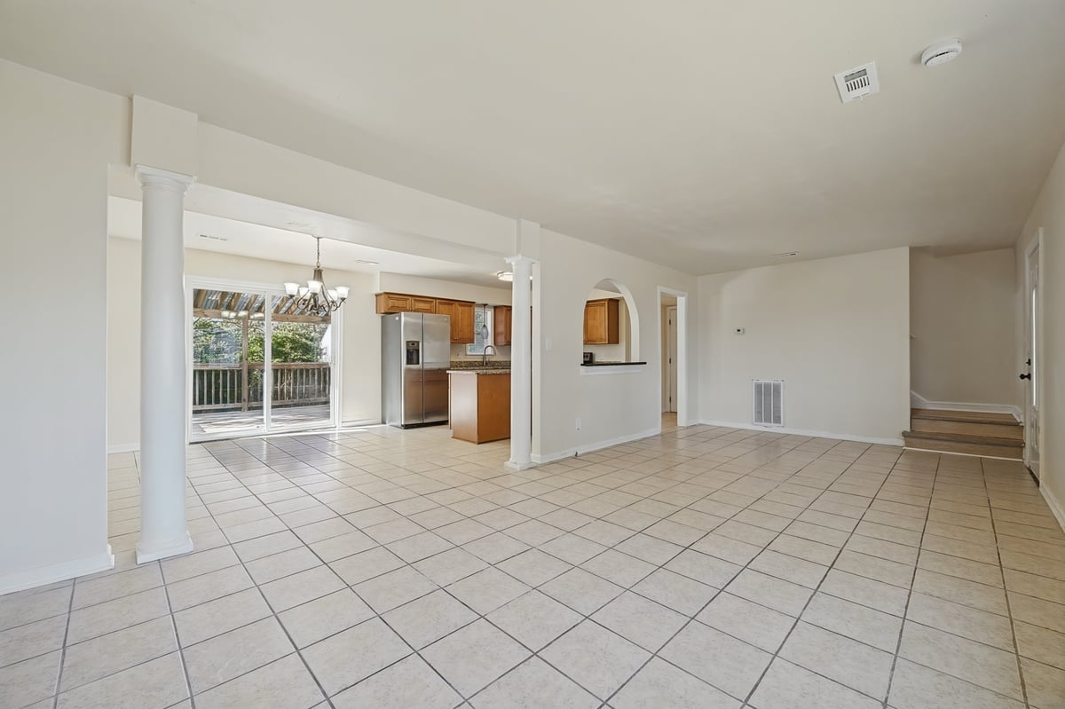 Spacious open-concept kitchen and living area with tile flooring, white walls, and glass doors leading to a covered patio