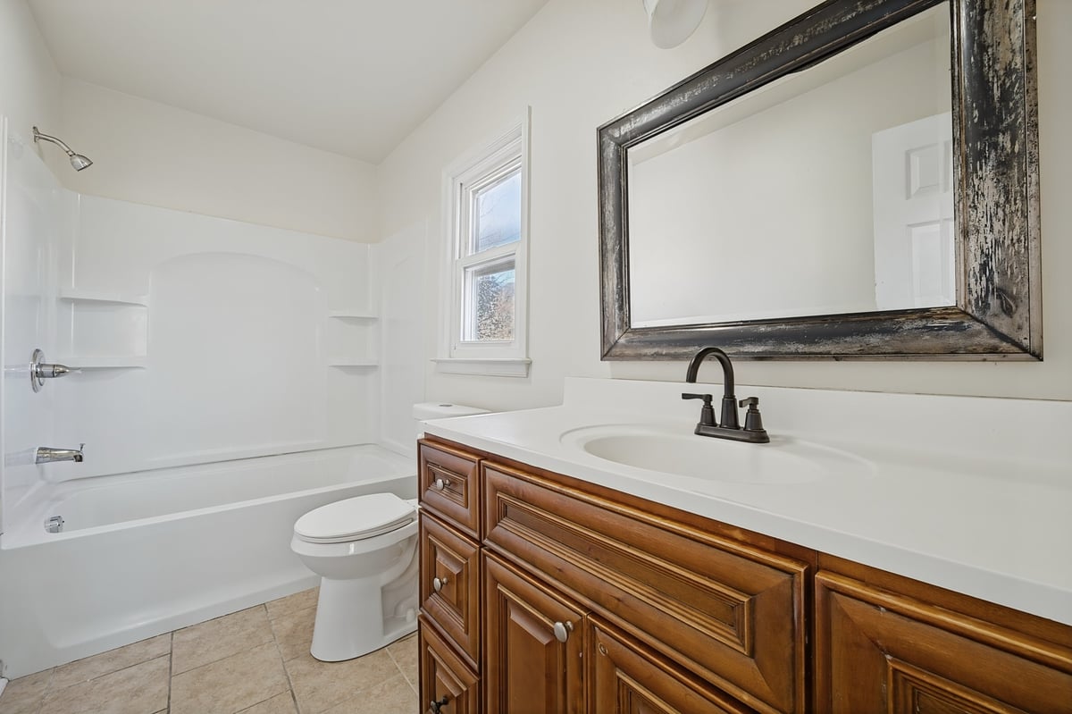 Modern bathroom with wood vanity, white countertop, framed mirror, and bathtub with white subway tile surround